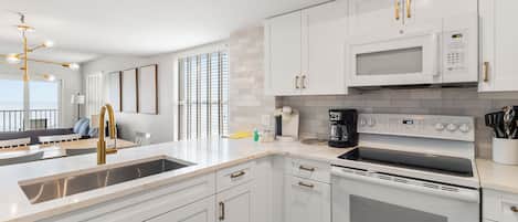 A modern kitchen with white cabinets, a stainless steel sink, a built-in microwave, and a stove.