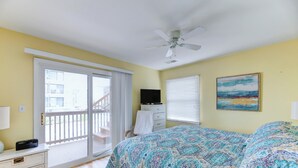 Ein Schlafzimmer mit Bett, Deckenventilator, Fernseher und Balkon mit Blick auf Gebäude.