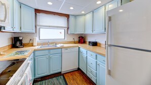 A kitchen with light blue cabinets, a white refrigerator, a sink, and a window with blinds.