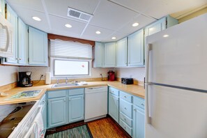 A kitchen with light blue cabinets, a white refrigerator, a sink, and a window with blinds.