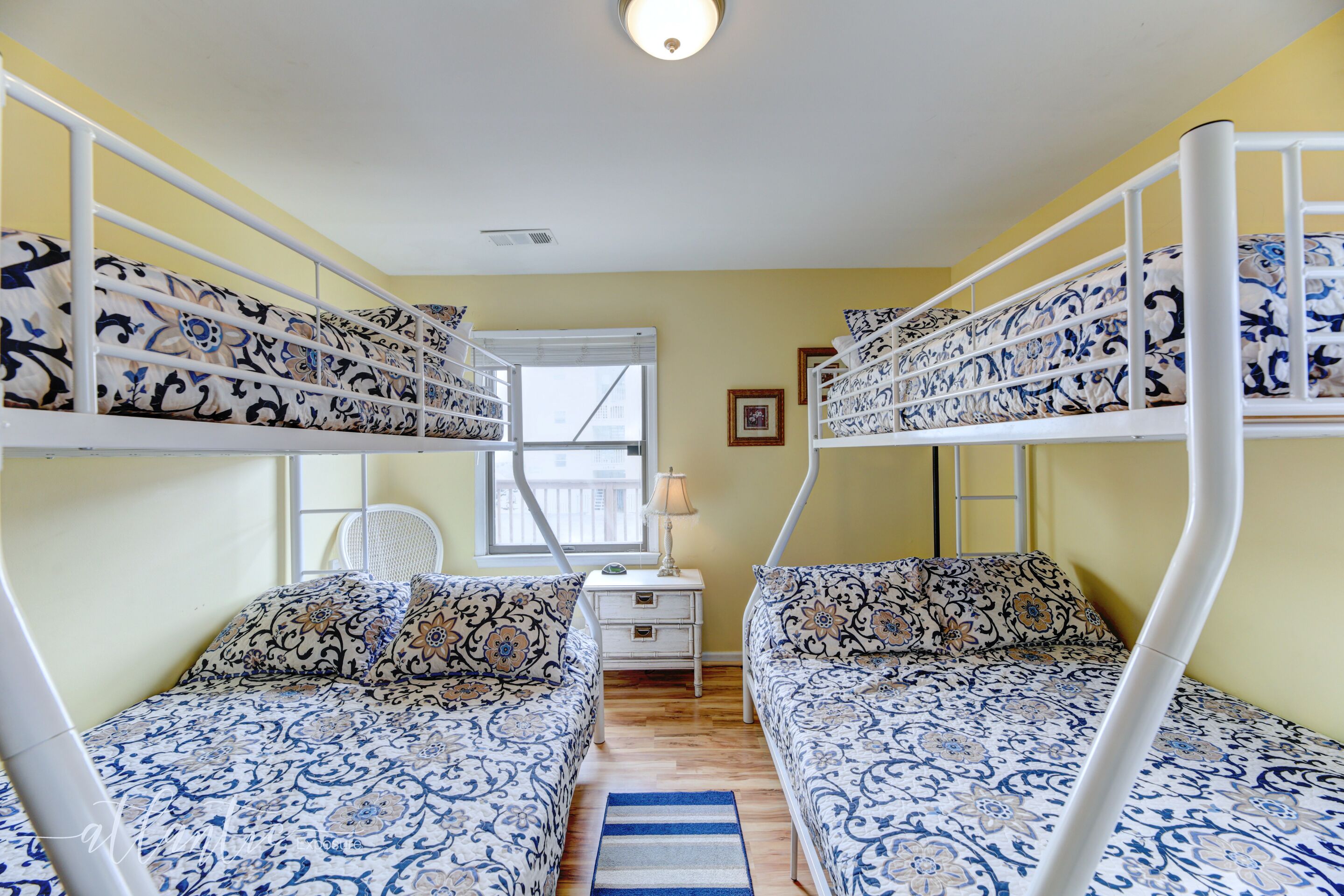 A room with bunk beds, a small bedside table, a lamp, and a window.