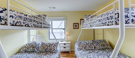 A room with bunk beds, a small bedside table, a lamp, and a window.