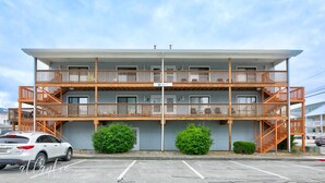 A multi-story motel with a flat roof, wooden balconies, and a parking lot in front.