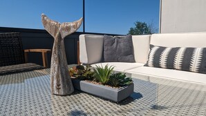 A modern outdoor seating area with a white sofa, patterned cushions, a decorative whale tail sculpture, and a planter with green plants. - Rooftop Views of the Space Needle & City (Seattle)