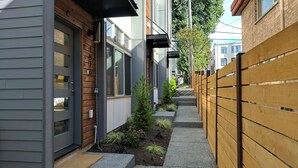 A narrow pathway flanked by a wooden fence and a building with a grey exterior and a wooden door. - Rooftop Views of the Space Needle & City (Seattle)