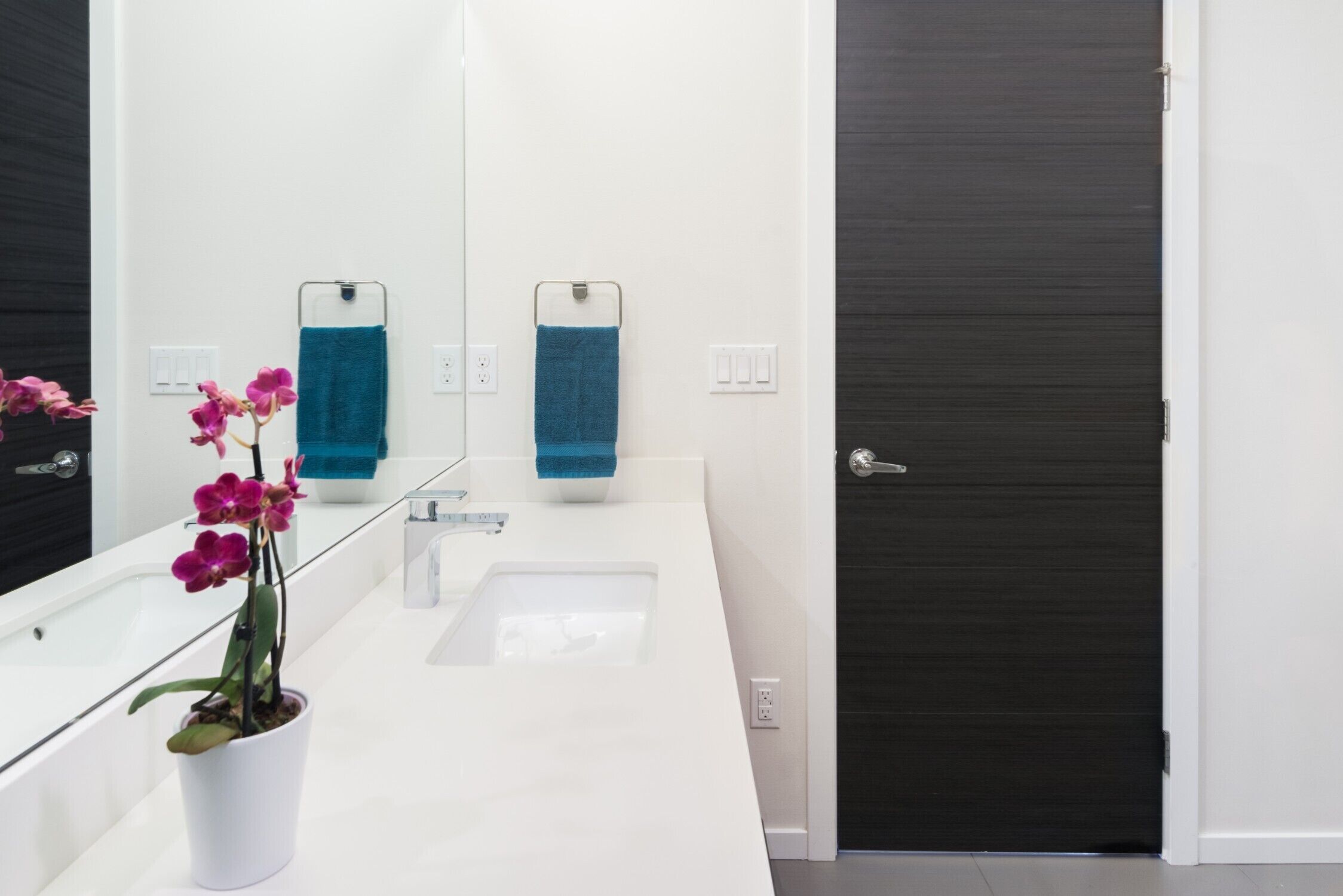 A modern bathroom with a white sink, a large mirror, and a potted orchid.