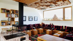 Uma sala de estar moderna com teto de madeira, estantes embutidas, lareira, janela ampla com vista e tapete estampado.