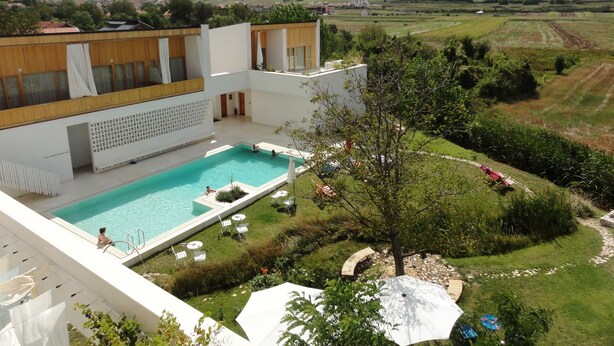 Um edifício moderno com piscina, rodeado por um jardim bem cuidado e uma vista panorâmica do campo.