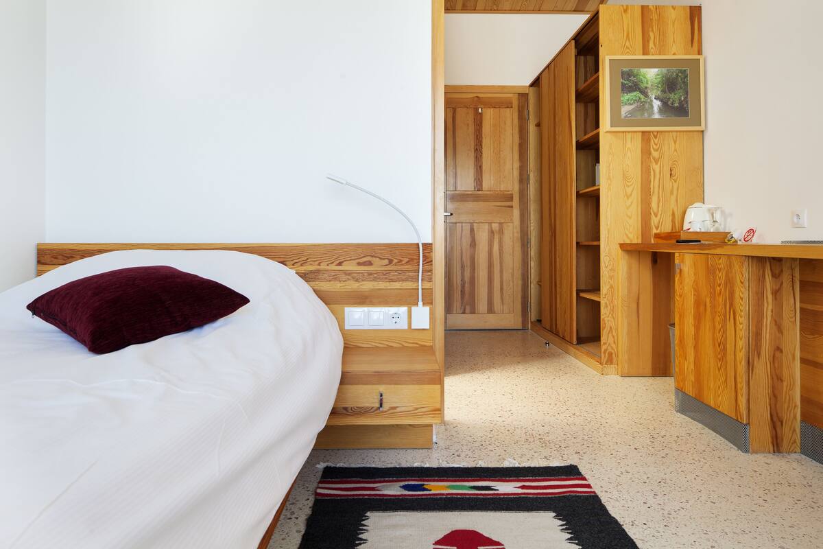 A bedroom with a bed, a wooden desk, and a wardrobe.