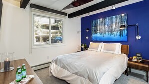 Un dormitorio con una cama grande, una ventana, un cuadro y una mesita de noche con una lámpara.