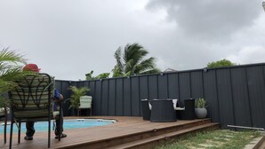 Un patio trasero con terraza de madera, una piscina y mobiliario exterior.