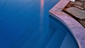 Une piscine avec vue sur le coucher de soleil, des marches en pierre et une côte lointaine.