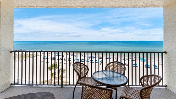 Un balcón con vista a la playa, sillas de mimbre y una mesa redonda.