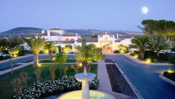 A well-maintained garden with a central fountain, palm trees, and a variety of shrubs. - Luxury 2 bedroom Frontline Golf Townhouse with shared pool in a gated community (Arcos de la Frontera)