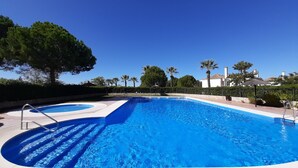 A swimming pool with a clear blue water feature, surrounded by a paved deck and a low stone wall. - Luxury 2 bedroom Frontline Golf Townhouse with shared pool in a gated community (Arcos de la Frontera)