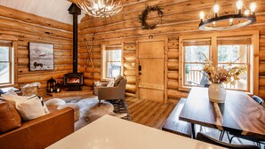 A log cabin interior with a fireplace, wooden walls, a chandelier, and a dining area. - Remodeled Fairplay Log Cabin w/ Wood-Burning Sauna (Fairplay)