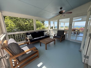 A covered porch with a sofa, two striped chairs, a wooden table, and a ceiling fan. - Classic waterfront cottage on Prudence Island, private beach, dock & mooring (Prudence Island)