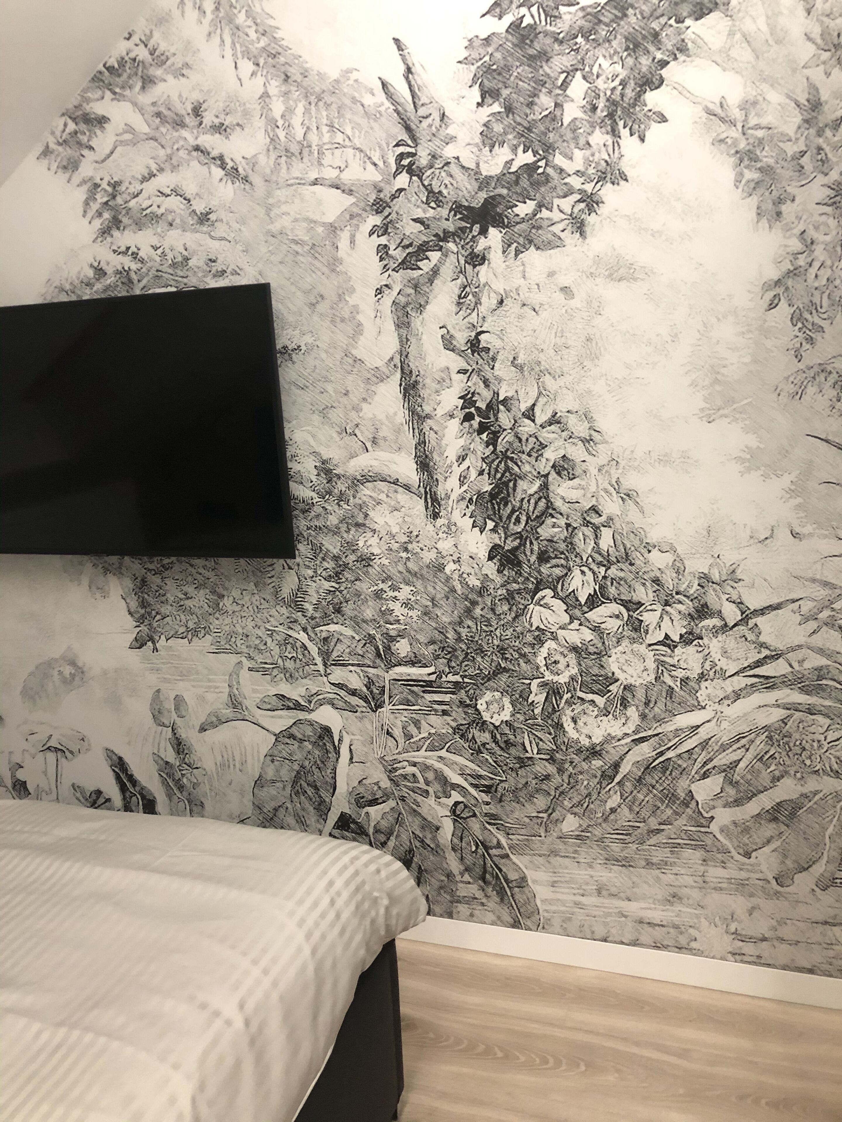 Un dormitori amb un llit, una televisió de pantalla plana penjada a la paret i un paper pintat amb un disseny detallat inspirat en la natura.