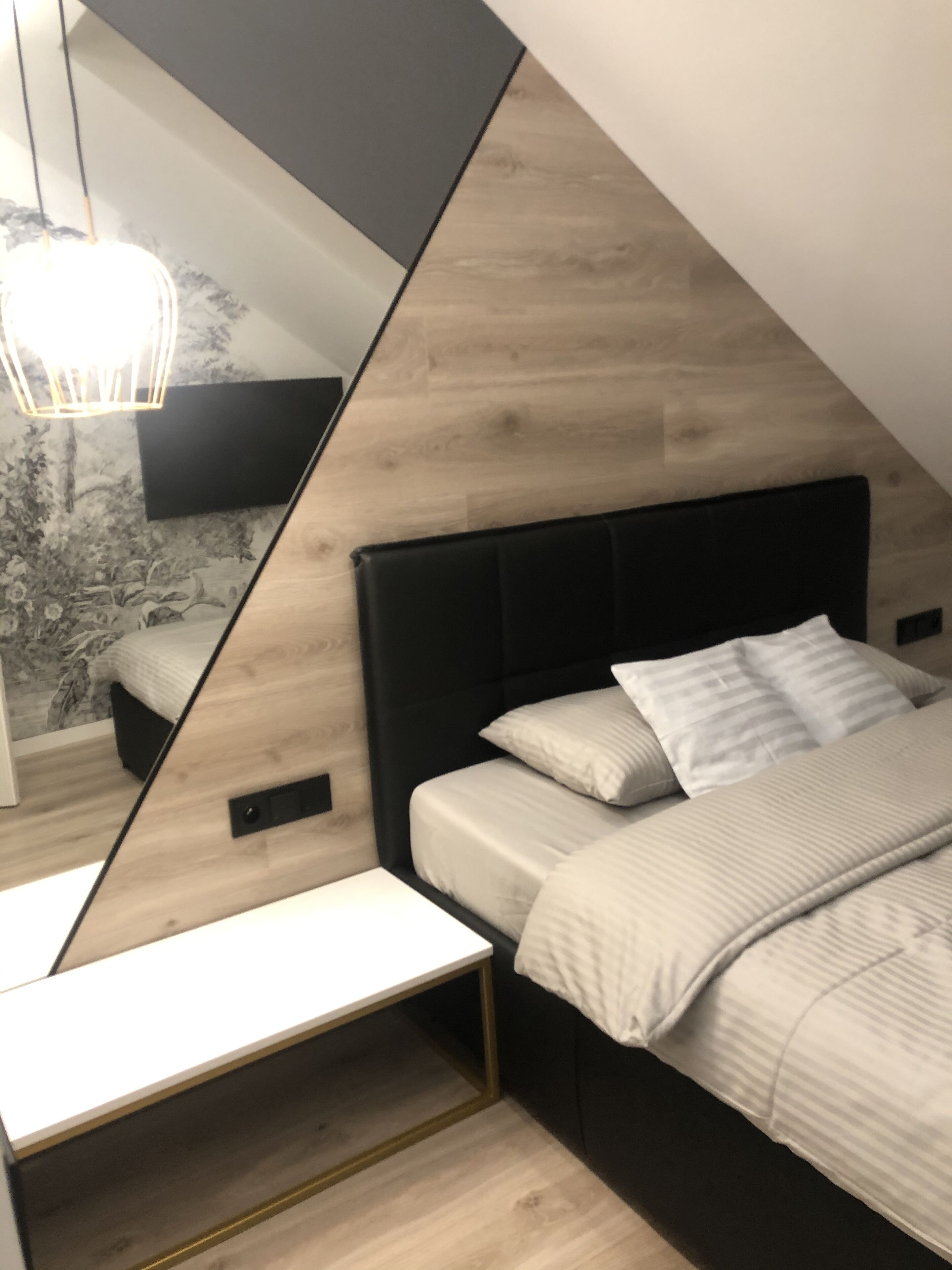 Une chambre moderne avec un lit, une table de chevet et un grand miroir qui reflète la pièce.