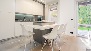A modern kitchen with white cabinetry, a central island, and a dining area with white chairs. - Premium Apartments in Wadowice (Wadowice)
