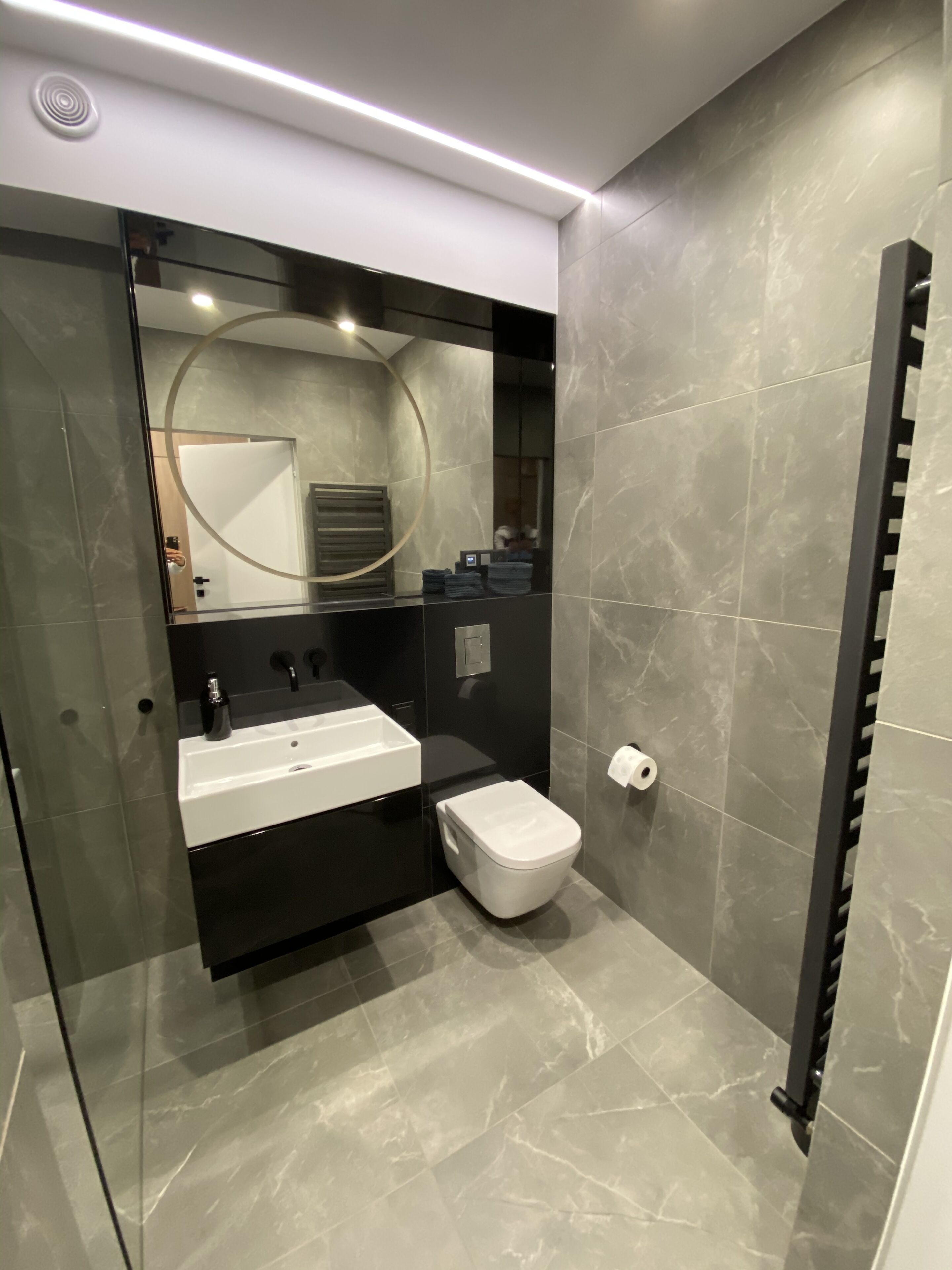 A modern bathroom with a glass partition, a white sink, a toilet, and a towel rack.