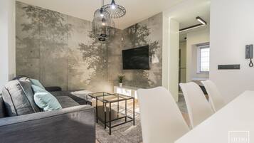 Una sala de estar moderna con un sofá gris, una mesa de centro de vidrio y un televisor montado en una pared con textura.
