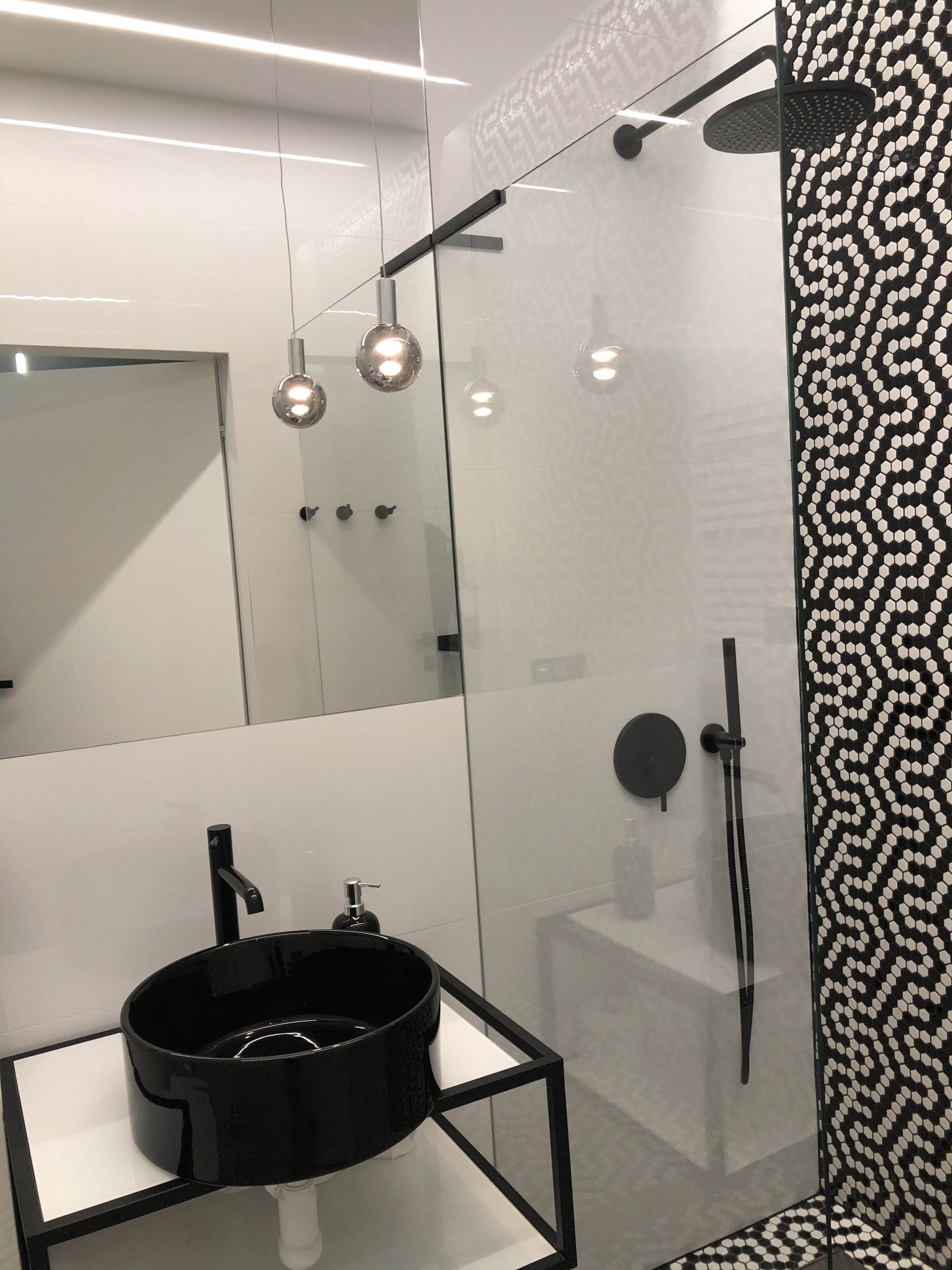 Un baño moderno con ducha envuelta en cristal, un lavabo negro sobre encimera blanca y pared con diseño.