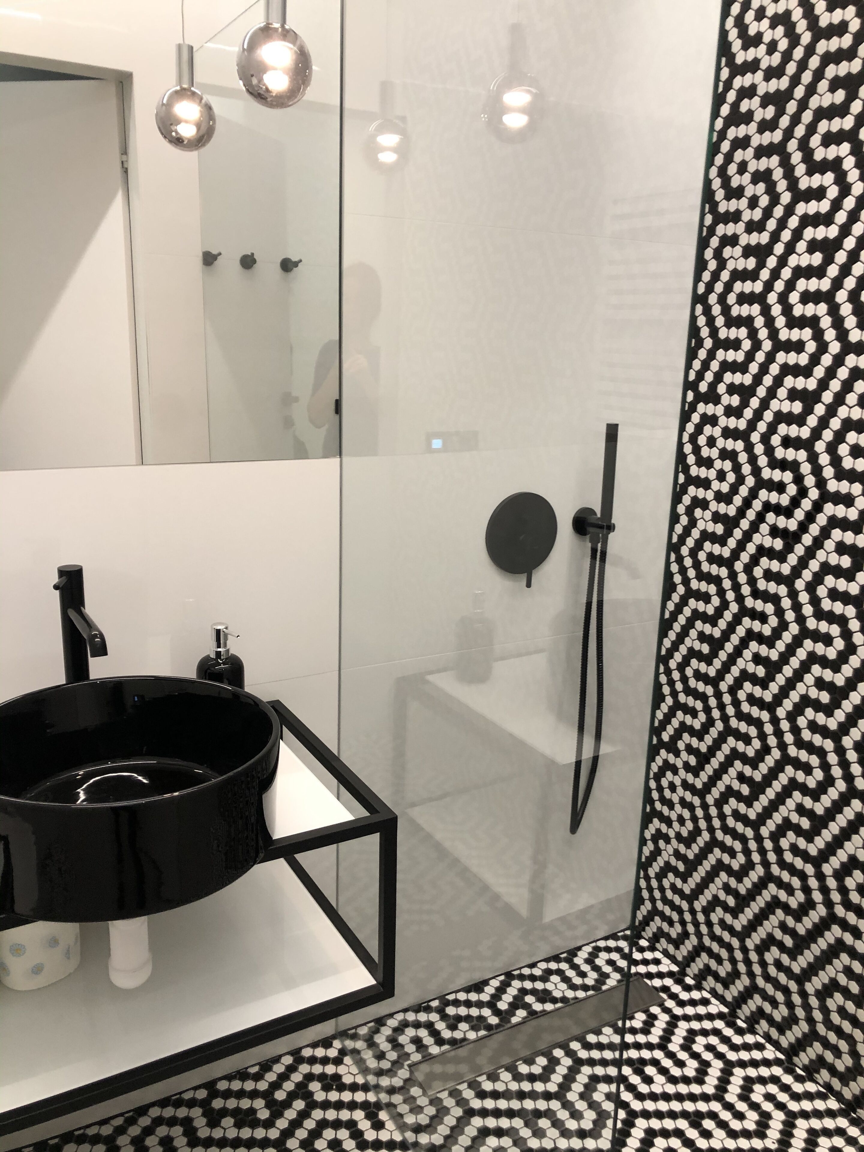 A modern bathroom with a black sink, a glass shower enclosure, and a patterned tile wall.