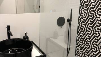 A modern bathroom with a black sink, a glass shower enclosure, and a patterned tile wall.
