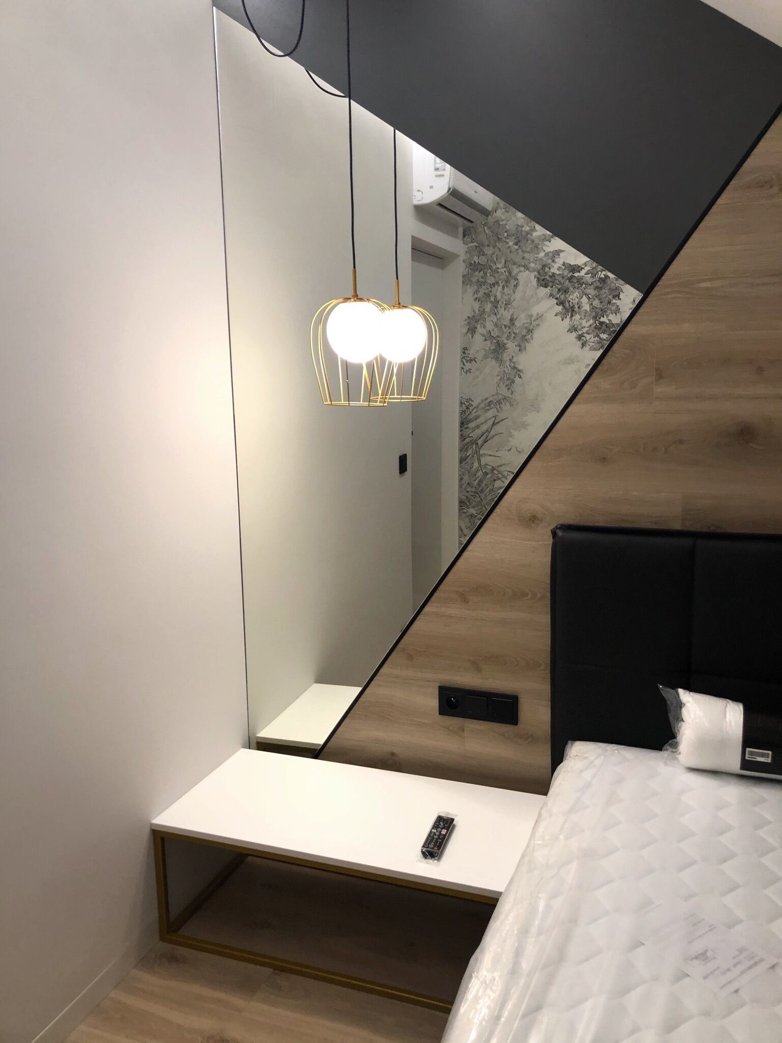 Un dormitorio moderno con un armario espejado, una mesita de noche con un control remoto y una lámpara de diseño único.