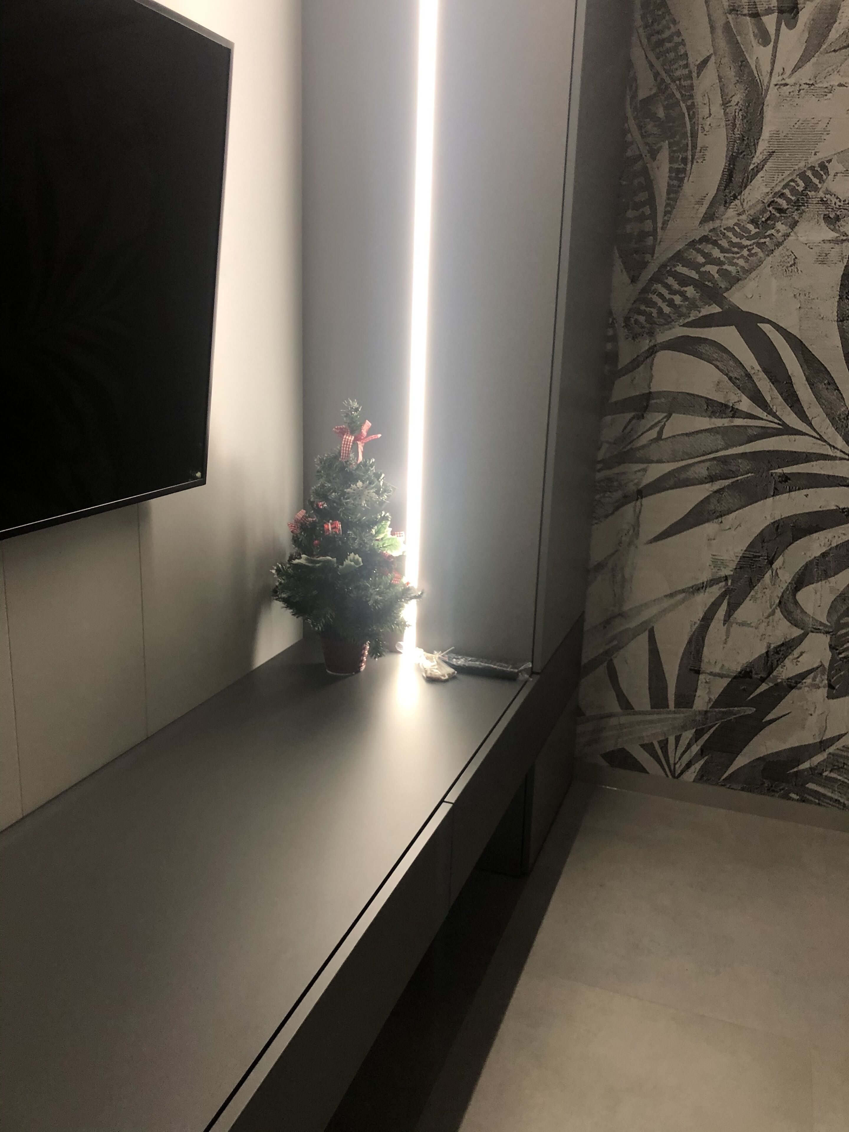 A corner of a room with a dark-colored bench, a small Christmas tree, and a patterned wallpaper.