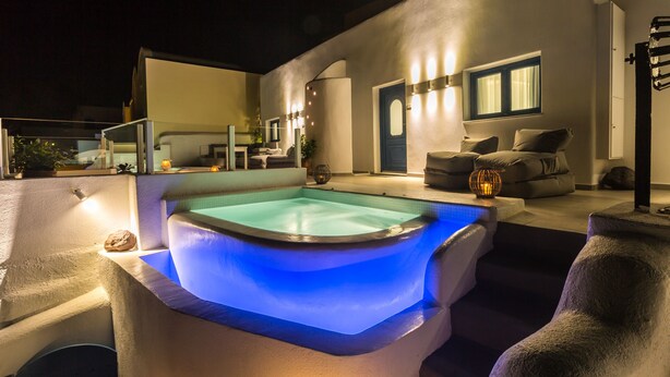 A hot tub with blue lighting, a seating area with cushions, and a poolside setting. - Amera Suites (Santorini)