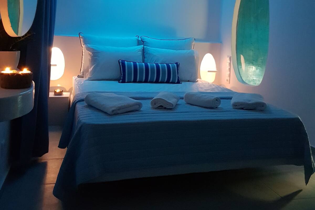 A modern bedroom with a curved ceiling, a bed with white linens and striped pillows, and two wall-mounted lamps.