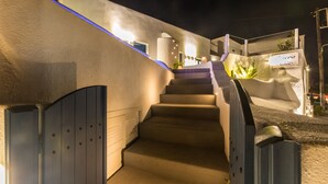 A nighttime view of a hotel entrance with a set of stairs leading up to a gated area. - Amera Suites (Santorini)