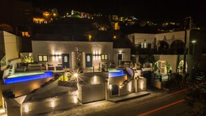 A modern hotel with a pool area, outdoor seating, and a well-lit entrance. - Amera Suites (Santorini)