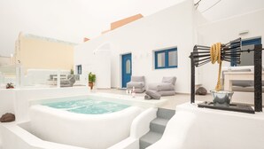 A modern, white-walled room with a hot tub, a small seating area, and a staircase leading to an upper level. - Amera Suites (Santorini)