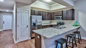 Una cocina moderna con armarios de madera oscura, un refrigerador de acero inoxidable, microondas empotrado, encimeras de granito y una isla central con taburetes de bar.