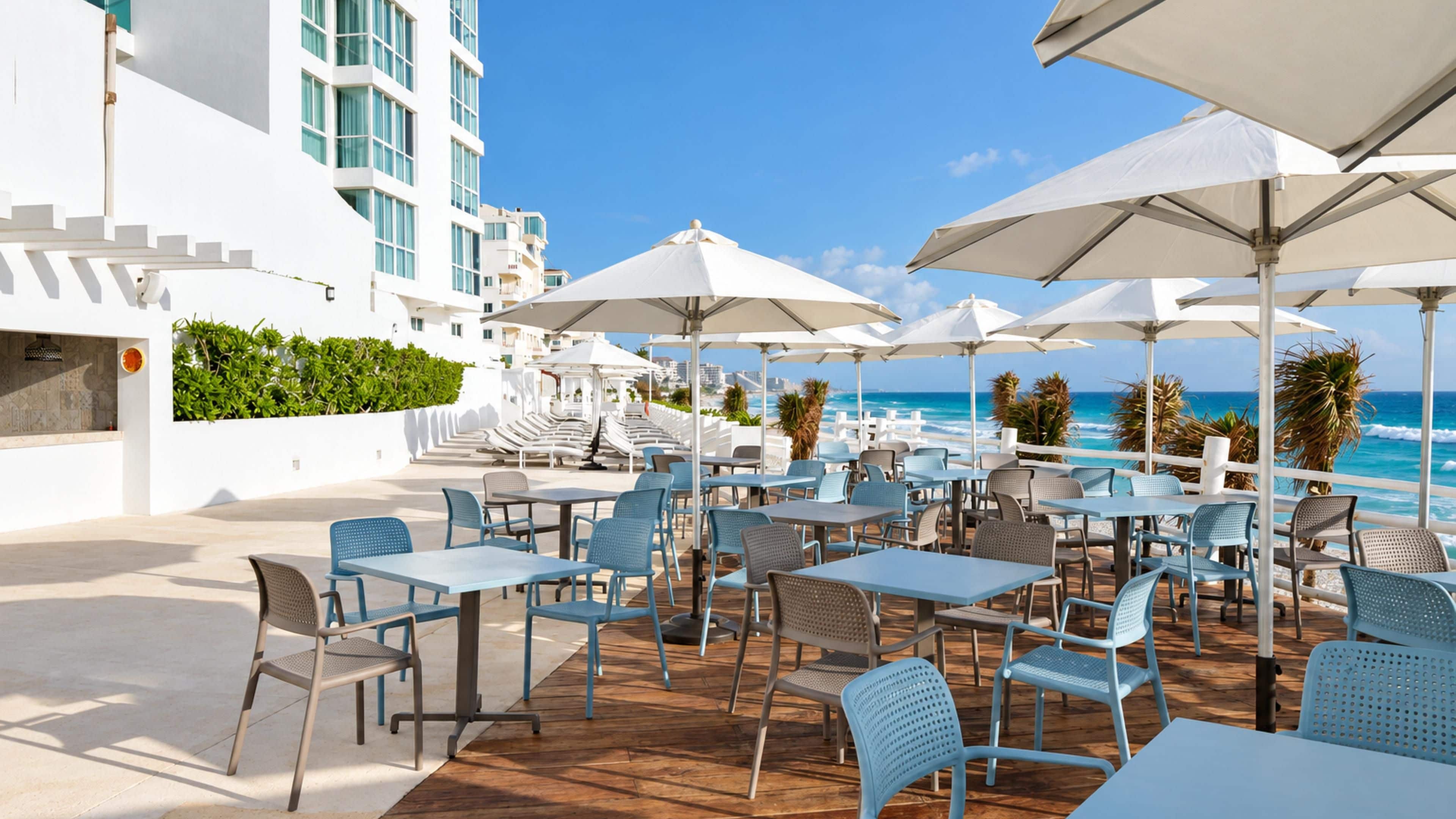 An outdoor seating area with tables and chairs, overlooking a beach and ocean.