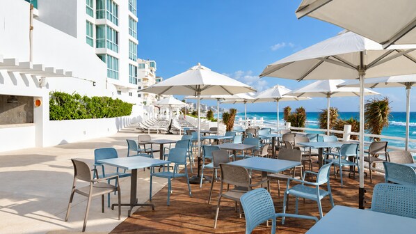 An outdoor seating area with tables and chairs, overlooking a beach and ocean.