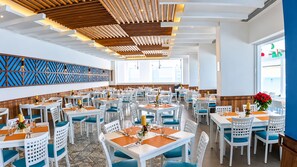 A spacious restaurant with white tables and blue chairs, featuring a modern ceiling design and a decorative wall panel.