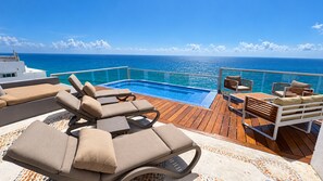 A sun deck with lounge chairs and a pool overlooking the ocean.