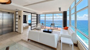 A modern living room with a large window overlooking the ocean, a white sofa, a coffee table, and a view of the sea. - There Can Be Only 1 Best Penthouse In all of Cancun!! (CANCUN)