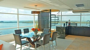 A modern kitchen with a view of the sea, a dining area with a glass table, and a staircase. - There Can Be Only 1 Best Penthouse In all of Cancun!! (CANCUN)