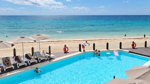 A pool area with lounge chairs and umbrellas, a lifebuoy, and a view of the beach and ocean.