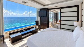 A modern hotel room with a large bed, a TV, a seating area with a view of the ocean, and a balcony.