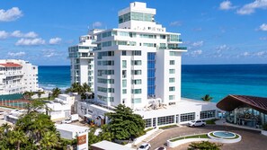 A modern hotel with multiple floors, a pool, and a view of the ocean.