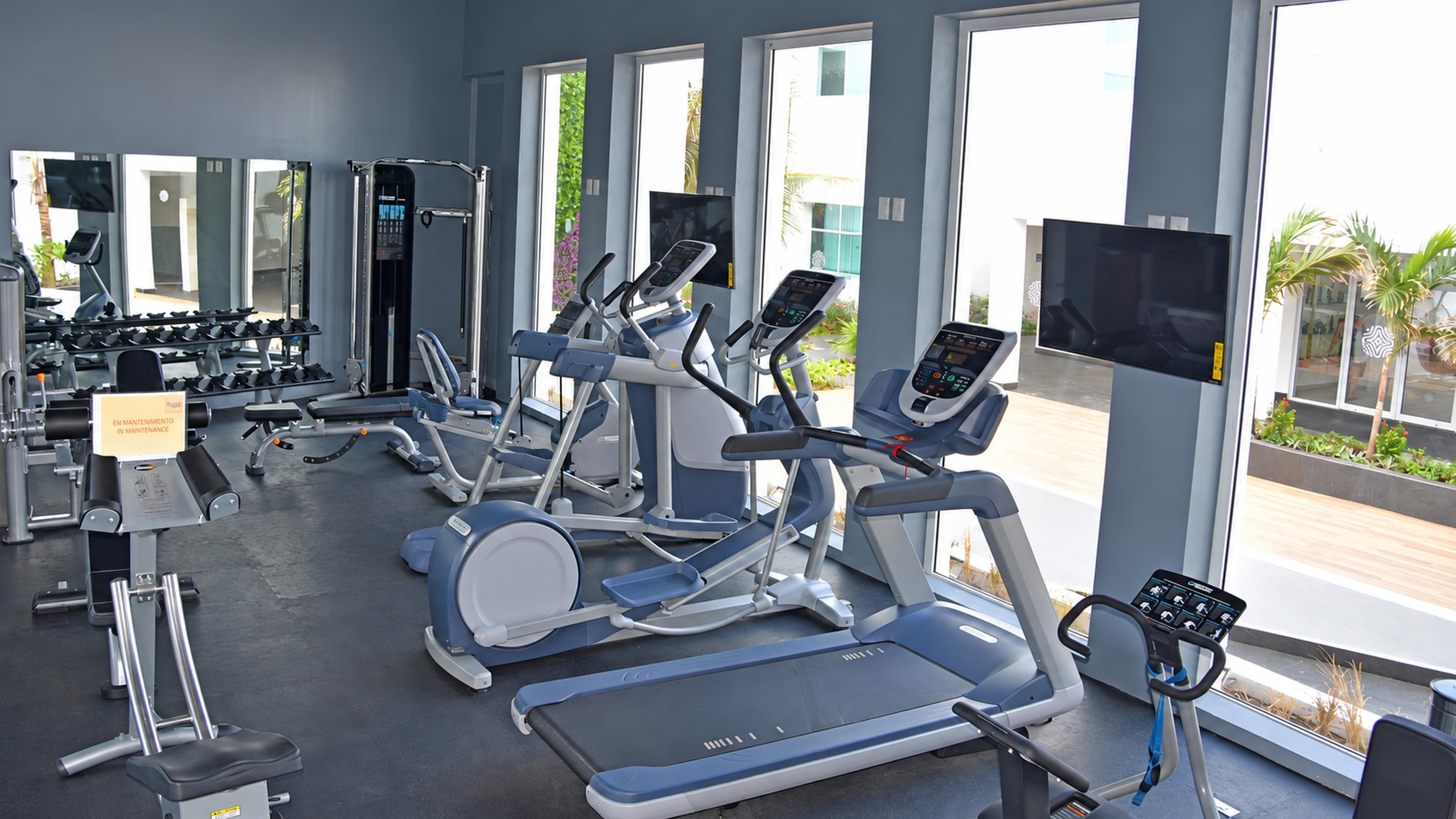 A gym with various exercise equipment, large windows, and a sign indicating maintenance.