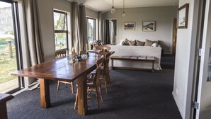 A spacious room with a large wooden dining table, a sofa, and a bed. There are large windows with curtains, a painting on the wall, and a view of the outdoors.