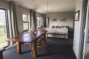 Amplia habitación con una gran mesa de madera para comer, un sofá y una cama. Cuenta con ventanas amplias con cortinas, un cuadro en la pared y vistas al exterior.
