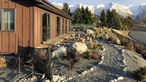 A wooden building with large windows, a gravel pathway, and a mountainous backdrop.